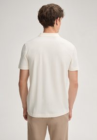 Weißes Polohemd mit kurzen Ärmeln, das über ein strukturiertes, geometrisches Muster verfügt. Es hat einen klassischen Kragen und einen dezenten geraden Saum. Eignet sich gut für die Freizeit.
