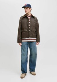 Giacca in cotone marrone con chiusura a zip, due tasche anteriori e colletto a contrasto, indossata sopra una maglietta a righe e abbinata a jeans blu.