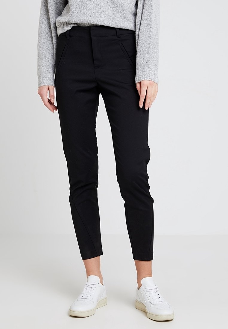 Svarta, slim-fit byxor med en slät textur, med sidofickor och en avsmalnande ben. Kombinerat med vita sneakers.