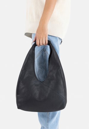 Zwart leren hobo tas met een gebogen bovenkant, een gladde textuur en zijnaaddetails, vastgehouden door een persoon tegen lichte kleding en denim.