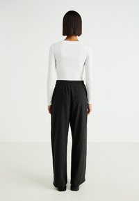 Striped black wide-leg pants with an elastic waistband, paired with a fitted white ribbed long-sleeve top. Minimalistic design.