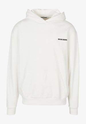 Balta kapuce ar kangarū poku. Uz kreisā krūškurvja ir melns logotipa teksts. Mīksts kokvilnas materiāls, brīvs griezums un ribotās piedurknes.