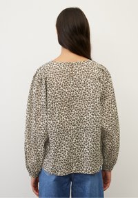 Blusa fiorata marrone e crema con maniche lunghe, scollatura rotonda e dettaglio a chiave sul retro. Tessuto morbido e leggero.