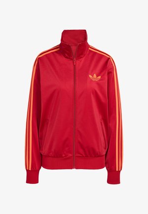Casaco atlético vermelho feito de tecido suave, com colarinho alto, dois bolsos laterais e detalhes em laranja com três riscas nas mangas.