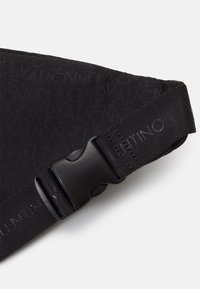 Svart slouch-väska med präglat logomönster, slitstarkt nylonmaterial, justerbar rem med plastspänne, strukturerad yta.