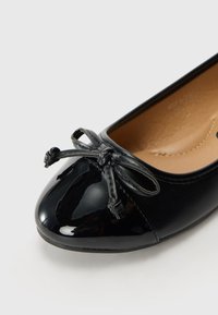 Sorte patent ballerina-flats med rund tå, teksturert lærdetalj og en dekorativ sløyfe foran. Glatt innvendig fôr.
