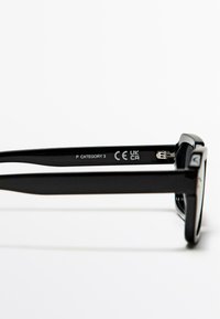 Czarne okulary przeciwsłoneczne z szerokimi plastikowymi oprawkami. Na wewnętrznej stronie zauszników znajdują się napisy "P KATEGORIA 3" oraz "CE UK CA". Gładka tekstura i elegancki design.