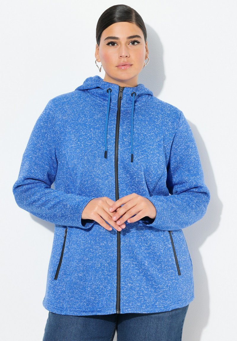 Blå huvjacka med en texturerad yta. Har en hel dragkedja och två sidofickor med svarta dragkedjor. Mjuk, avslappnad design.