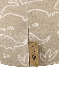 Light beige fabric with white animal and plant patterns. Features a stitched seam and a small brown label with text at the edge.
