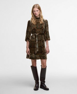 Groene jurk met paisley-patroon, lange pofmouwen, een strakke taille en een lengte tot de knie. Gecombineerd met bruin leren laarzen tot de knie.