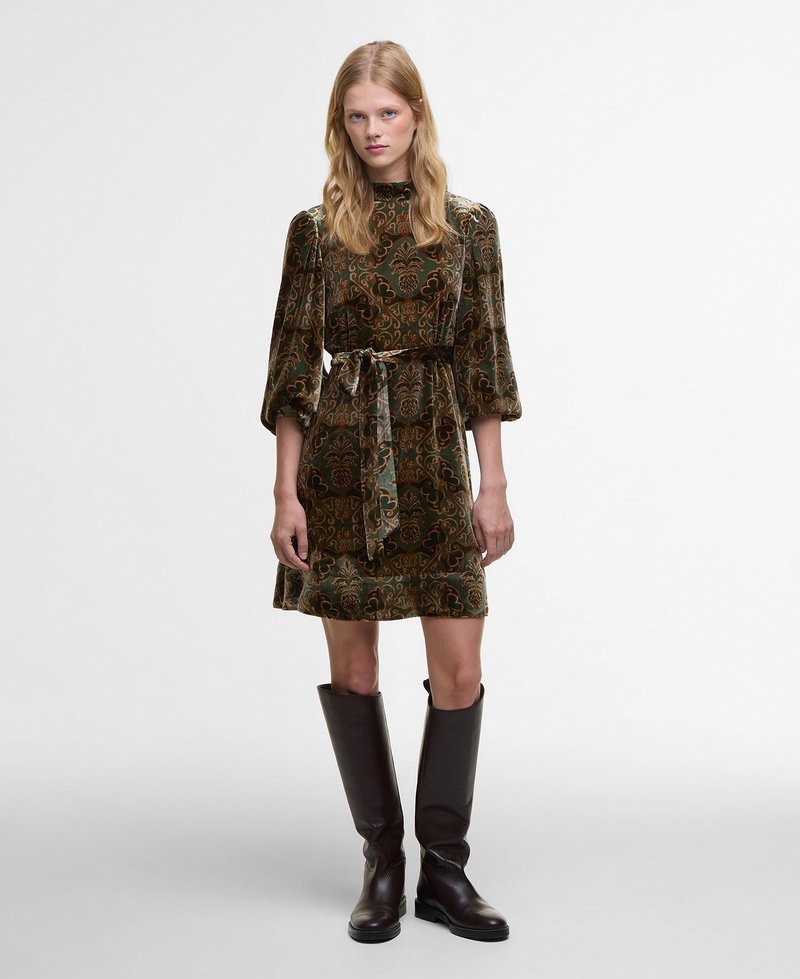 Robe verte à motifs paisley avec des manches bouffantes longues, taille cintrée et ourlet jusqu'aux genoux. Associée à des bottes en cuir marron montantes jusqu'aux genoux.