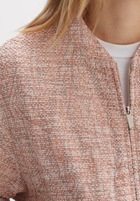 Roze textuur bomberjack met een rits sluiting, zachte stof met een geweven patroon en contrasterende licht en donkerdraad details.