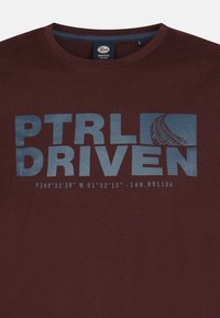 Bordová bavlnená tričko s modrou grafickou potlačou a textom "PTRL DRIVEN" a súradnicami pod ním, s okrúhlym výstrihom a krátkymi rukávmi.