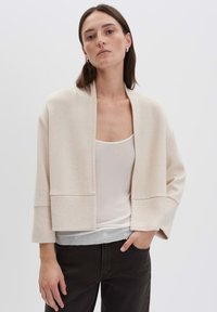 Beige oversized Cardigan aus weichem Material, cropped Design mit weiten Ärmeln, minimalistischer Silhouette und ohne Verschlüsse.