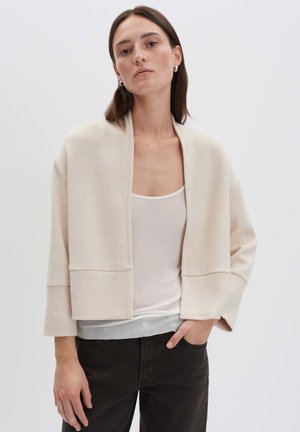 Cardigan oversize beige in materiale morbido, design cropped con maniche ampie, caratterizzato da una silhouette minimalista e senza chiusure.