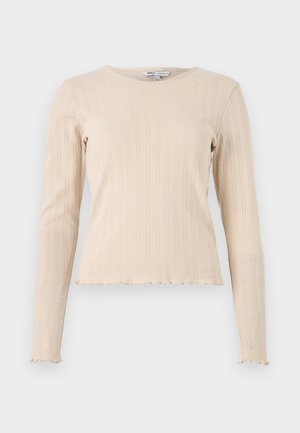 Beige long-sleeve ribbed top with a round neck and scalloped hem. Fabric features a subtle textured pattern throughout.
