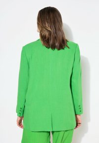 Grön linneblazer med en strukturerad design, enkel sprund och tre knäppta manschetter. Tyget har en slät, texturerad yta.