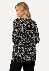 Zwarte top met een all-over print van cijfers in crème. Relaxte pasvorm met driekwart mouwen en een ronde halslijn. Soepele textuur.