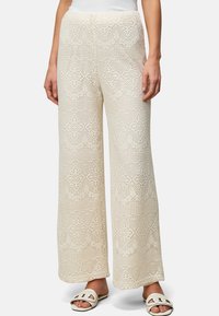 Pantalons larges en crochet blanc crème, ornés de motifs délicats semblables à de la dentelle et d'une surface texturée, associés à des sandales plates.