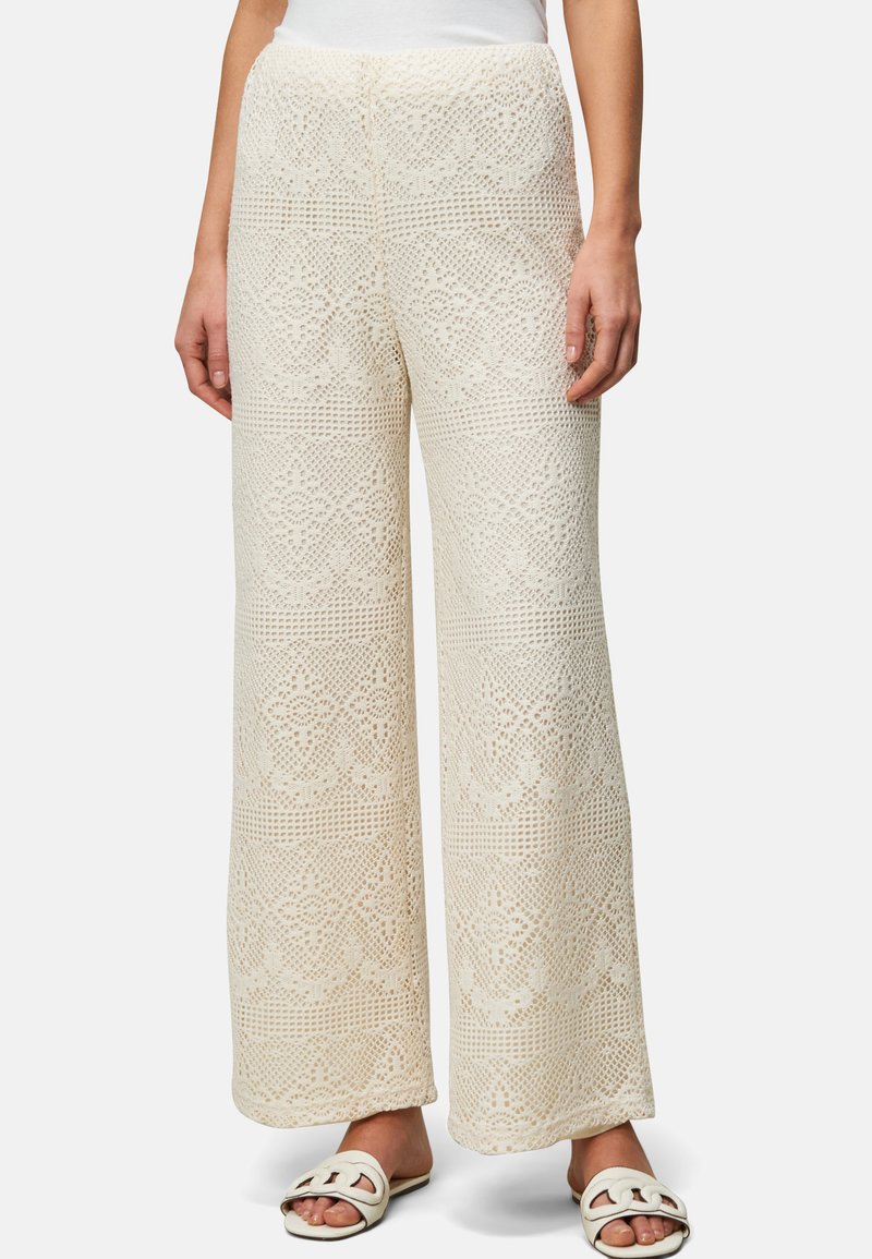 Pantalons larges en crochet blanc crème, ornés de motifs délicats semblables à de la dentelle et d'une surface texturée, associés à des sandales plates.
