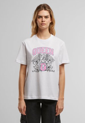 Jeune femme aux cheveux blonds porte un t-shirt blanc avec un texte rose "QUEEN" et un graphisme noir représentant un oiseau et deux lions.