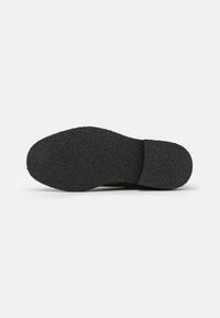 Suela de zapato de goma negra con un acabado texturizado y bordes redondeados. Presenta una base plana para estabilidad y agarre.