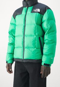 Zelená pufovaná bunda s černými akcenty, se zipem vpředu, vysokým límcem a prošívaným vzhledem. Obsahuje boční kapsy a detaily loga.