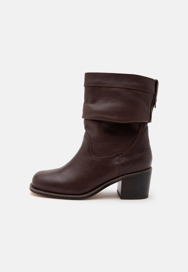 Bottine en cuir brun foncé avec revers plié et talon bloc, montrée de profil sur un fond clair uni.