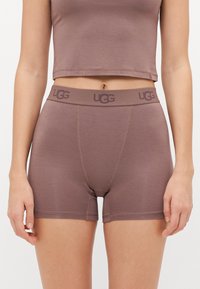 Smeđe UGG bokserice s pojasom sa logotipom, izrađene od mekog materijala, s ravnim šavovima i prilagođenim dizajnom.