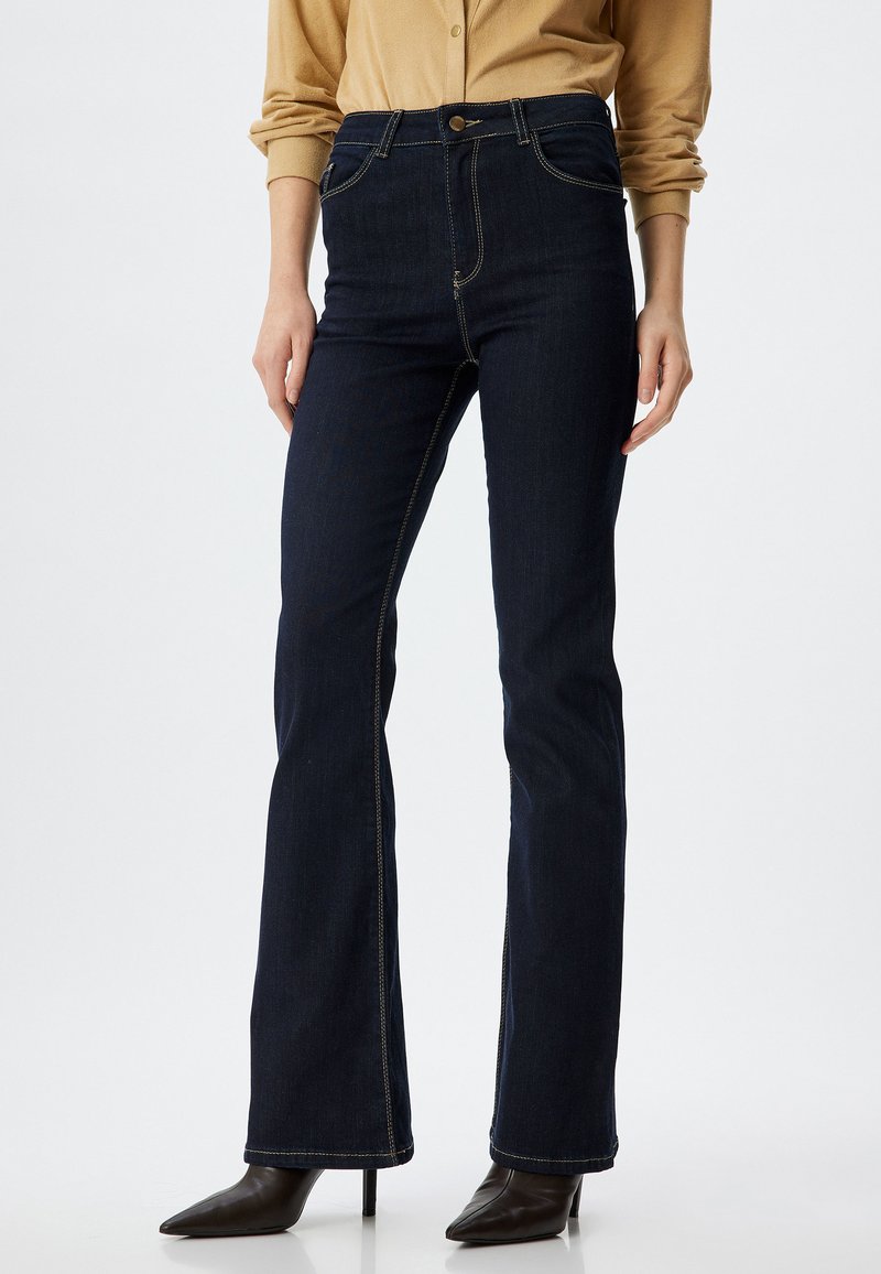 Jeans svasati blu scuro con vita alta, con cuciture a vista, cinque tasche e chiusura con bottone frontale. Tessuto in denim liscio.