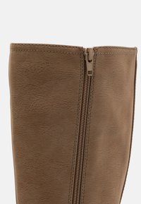 Botte synthétique marron montante avec une finition texturée, une fermeture éclair sur le côté et des accents cousus le long des coutures.