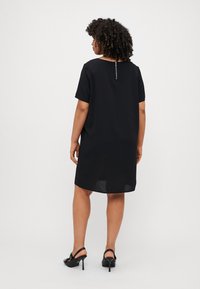 Robe noire à manches courtes, avec une coupe ample, un col rond et une fermeture éclair visible dans le dos. Tissu lisse et design jusqu'au genou.