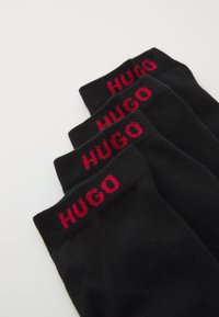 Chaussettes en coton noir avec le logo "HUGO" en rouge tricoté en haut. Texture lisse, longueur mi-mollet et design simple.