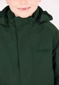 Groene lichtgewichtjas met capuchon, voorzien van een ritssluiting aan de voorkant en een reliëflogo op de borst. Het materiaal lijkt glad en duurzaam.