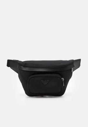 Sac banane en nylon noir avec poche avant zippée et emblème logo argenté, sangle ajustable et fermeture éclair supérieure.