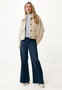 Krémová zateplená krátká bunda z vlněné směsi s velkými kapsami a knoflíky, spárovaná s tmavými zvonovými džíny s vysokým pasem a krémově bílými podpatky.