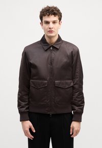 Veste bombardier marron en tissu lisse, dotée d'un col, d'une fermeture éclair frontale, de deux poches poitrine et de poignets et d'un ourlet côtelés.