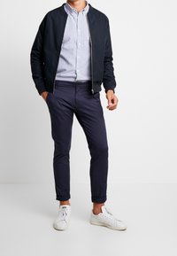 Marine bomberjack over een wit en blauw gestreept shirt, gecombineerd met opgerolde marine chino's en witte sneakers, met een rits aan de voorkant.