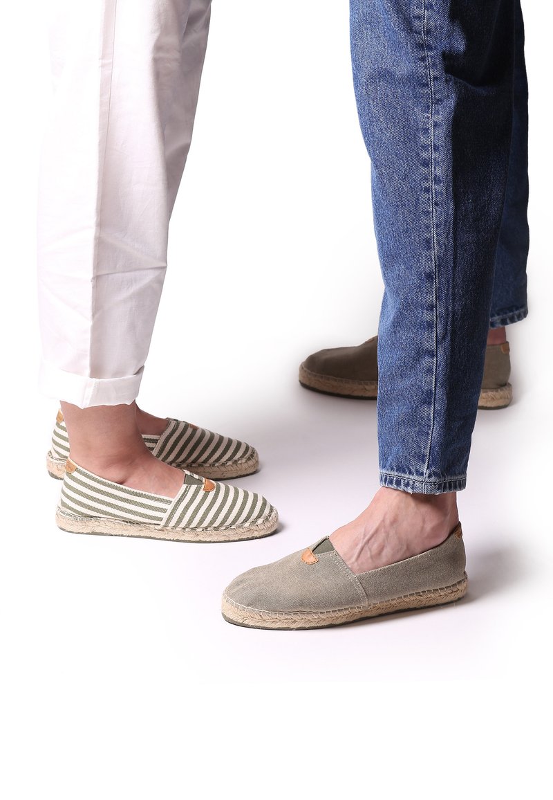 Randiga gröna och vita canvas-espadriller med brunt accent och jutesulor, tillsammans med grå canvas-espadriller, sedda från mitten av vaden och ner.
