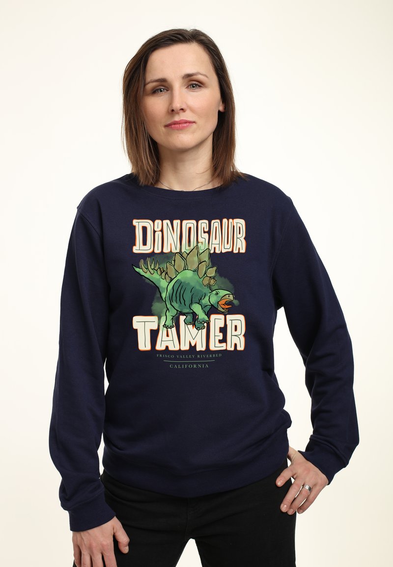 Felpa blu navy con grafica di un dinosauro e la scritta "Domatore di Dinosauri". Realizzata in tessuto morbido, con polsini a coste e una vestibilità rilassata.