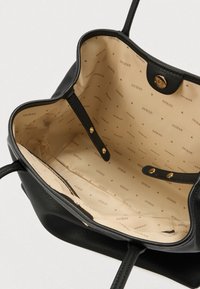 Melna ādas rokassoma ar teksturētu ārpusi, iekšpusē ar bēša krāsas oderi, kurā atkārtojas "Guess" logotips un mazas trīsstūra formas.