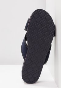 Sandale bleu marine avec tige en tissu et semelle extérieure en caoutchouc noir texturé. Dotée d'un design à lanières croisées et d'un motif de crampons prononcé sur la semelle.