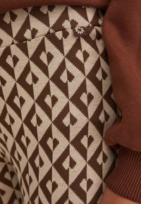 Bruna mönstrade leggings med ett geometriskt mönster som har hjärtan. Tyget är stickat och kompletteras av en ärm i rostfärg.