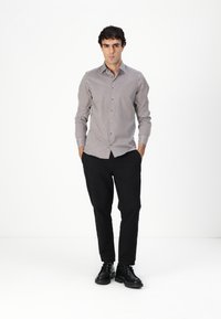 Chemise à manches longues pour homme en blanc avec un motif en losanges noirs, associée à un pantalon noir et des chaussures noires. Fermeture à boutons sur le devant et coupe ajustée.