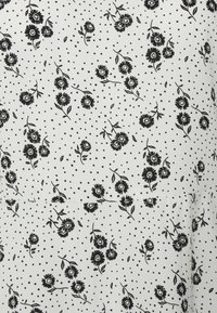 Tecido branco com padrão floral preto e bolinhas pretas espalhadas. Apresenta flores contornadas com folhas sobre uma superfície texturizada.