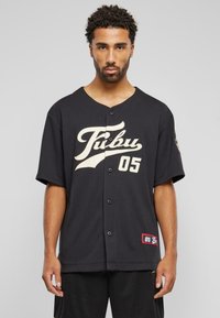 Jersey scurt negru cu mâneci scurte, având un logo crem și numărul "05" pe față, cu o textură subtilă și nasturi pe mijloc.