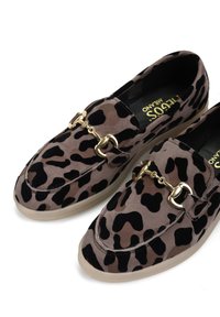 Mokasyny w panterkę wykonane z zamszu, z akcentem w postaci złotego łańcucha, okrągłym noskiem i beżową gumową podeszwą. Teksturowana powierzchnia z czarnymi plamkami.