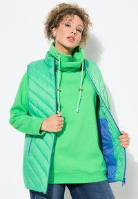 Chaleco verde con capas y un patrón acolchado, combinado con una sudadera verde a juego que presenta un cuello alto y cordones.