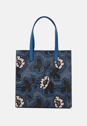 Blå og sort blomsterprintet tote taske med lyserøde blomster og lange blå håndtag, vist mod en ensfarvet baggrund.