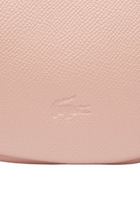 Sac en cuir rose avec une surface texturée, présentant un logo en relief subtil. Forme arrondie avec une finition lisse.